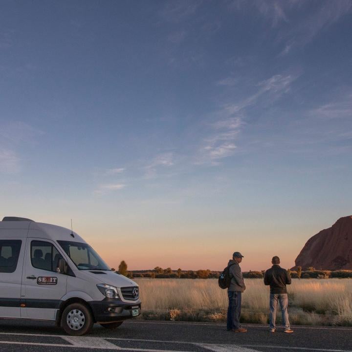 A couple standing beside a van with Ayers Rock in the background