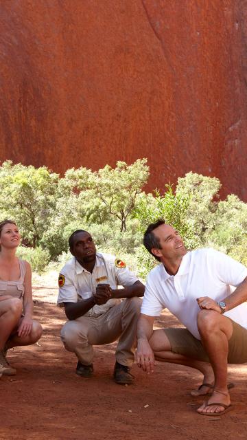 people crouched in the shadows of Ayers Rock