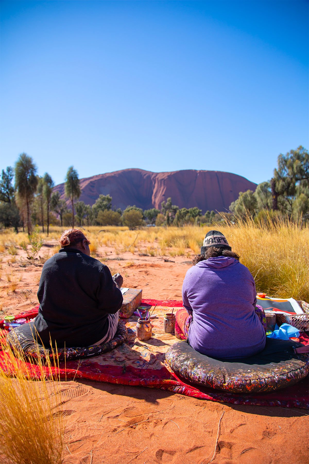 two people sitting on blankets in the outback