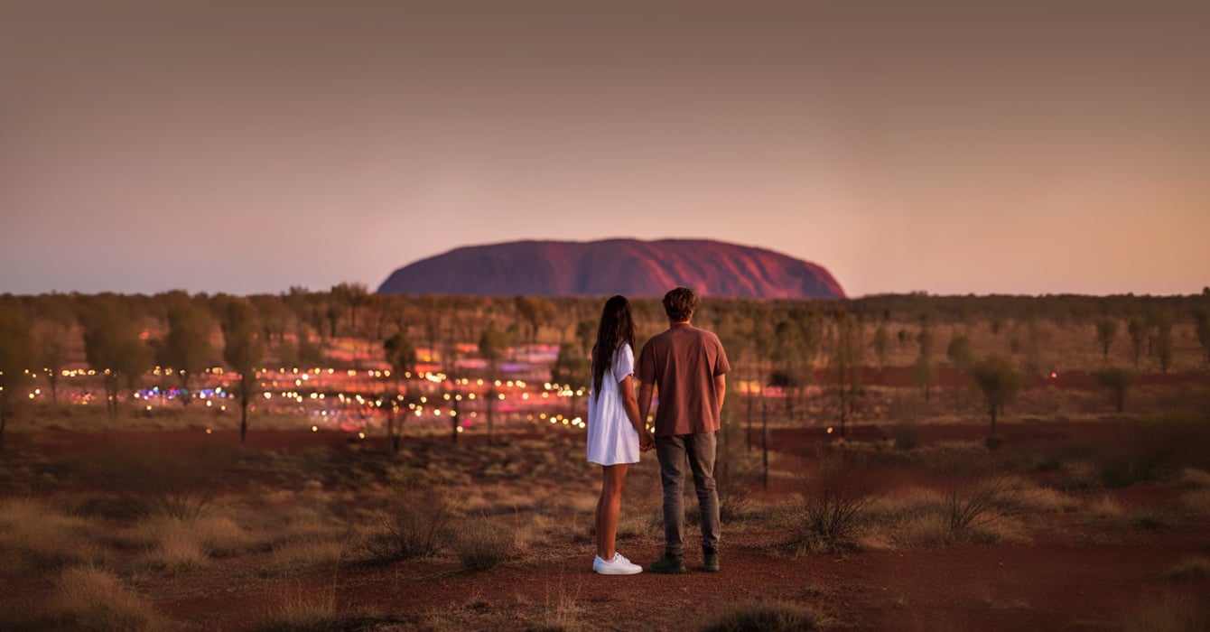 Couple standing in front of the Field of Light exhibition with Uluru in the background