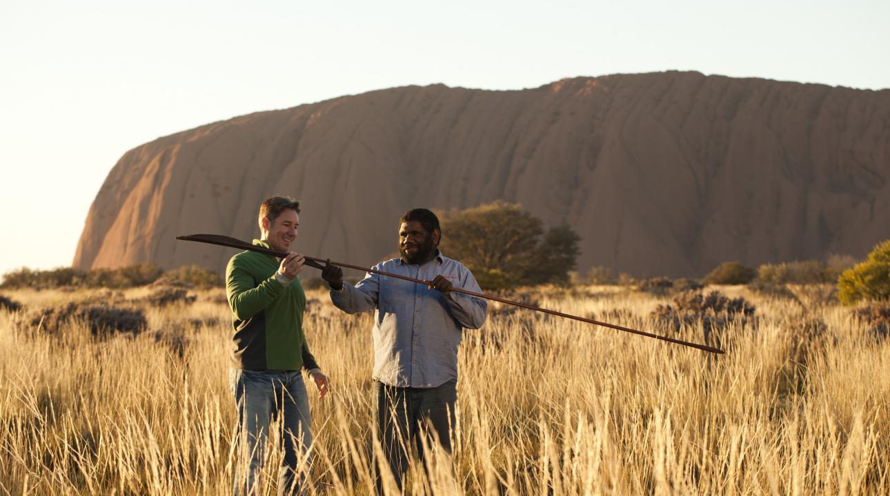 an indigenous man showing a tourist an atlatl