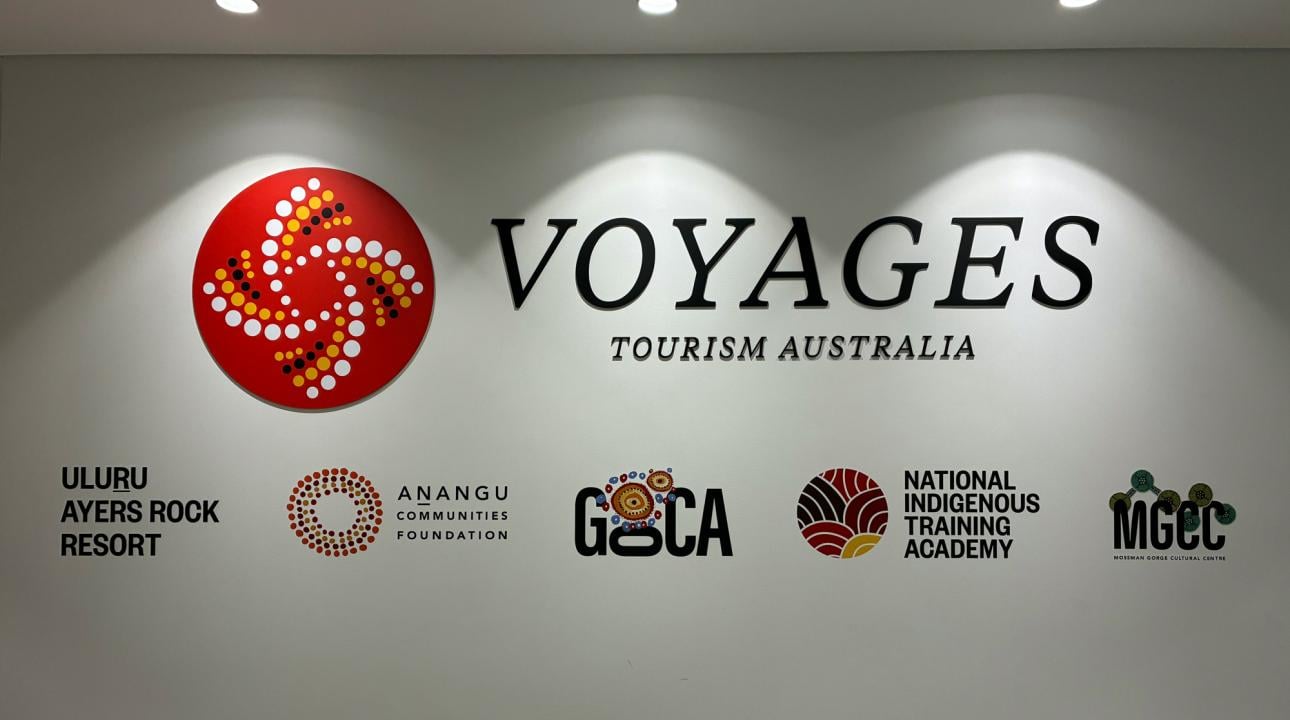 A sign for Voyages Tourism Australia and its collection of brands, including Uluru Ayers Rock Resort, Anangu Communities Foundation, Gallery of Central Australia, National Indigenous Training Academy, and Mossman Gorge Cultural Centre
