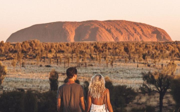 two people walking in the outback with Ayers Rock in the distance