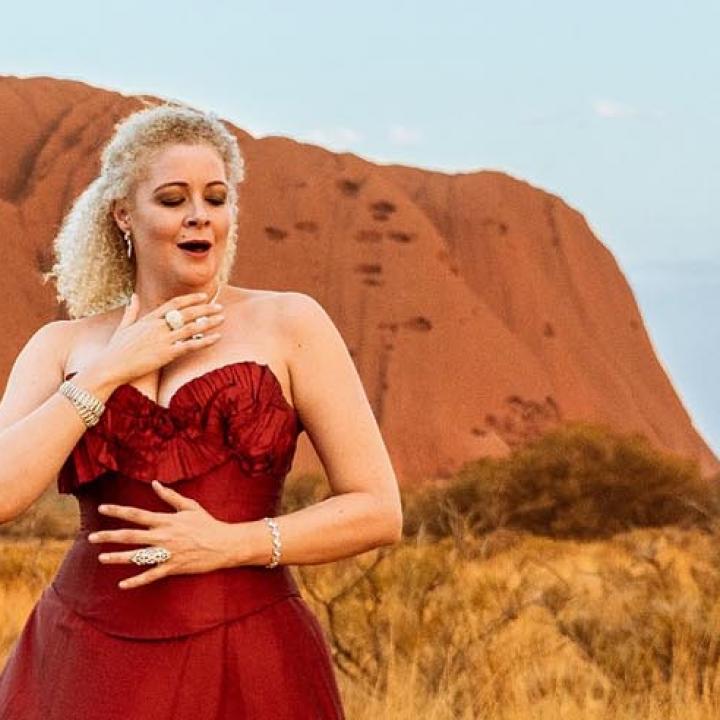 Opera singer in red gown in front of Uluru Ayers Rock