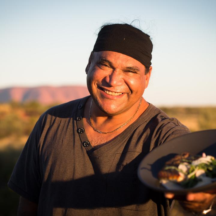 Chef Mark Olive presenting a dish in front of Uluru