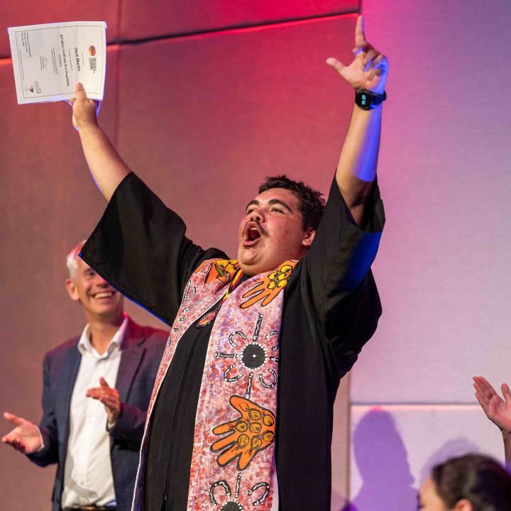 A NITA graduate with their hands up holding their certificate and people clapping in the background