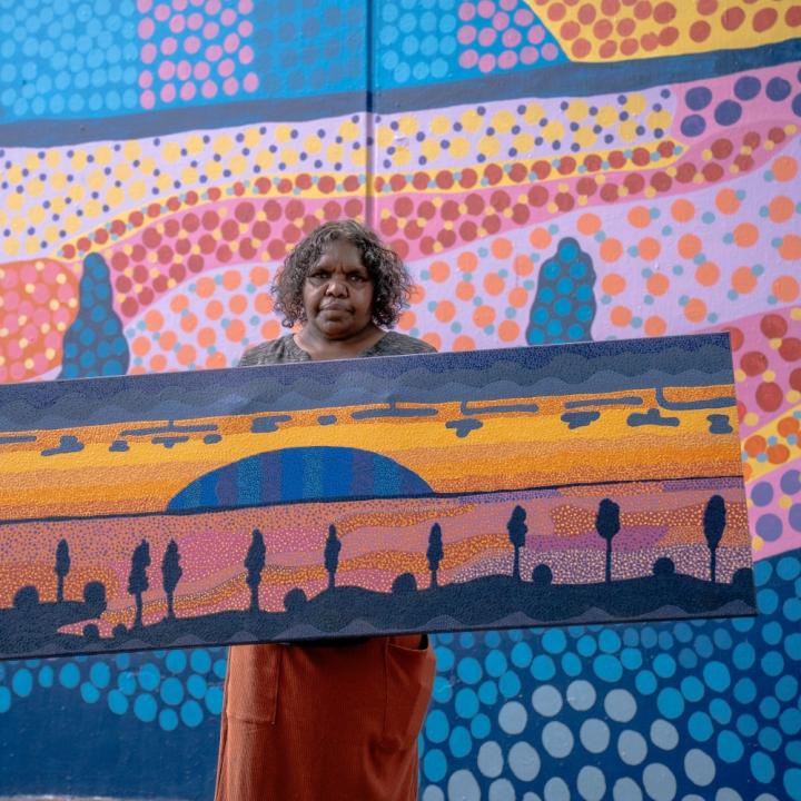 Indigenous artist Valerie Brumby holding her original dot painting artwork depicting the Field of Light at Uluru