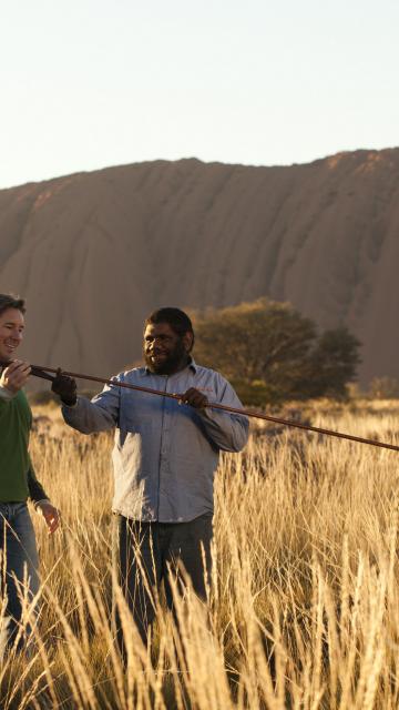 an indigenous man showing a tourist an atlatl