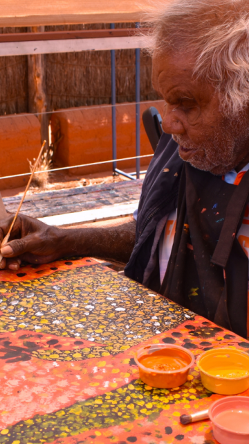 Reggie Uluru sitting down and painting on a large canvas