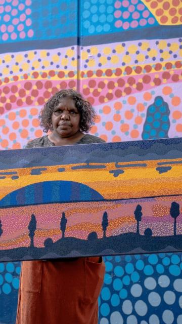 Indigenous artist Valerie Brumby holding her original dot painting artwork depicting the Field of Light at Uluru