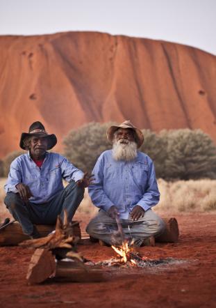 Two Anangu men sit by a fire